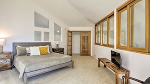 Ein Schlafzimmer mit einem Bett, einem Fernseher, einer hölzernen Bank und einer Tür zu einem anderen Raum.