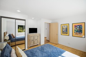 A bedroom with a bed, a television, a wardrobe, a mirror, and two framed posters on the wall.