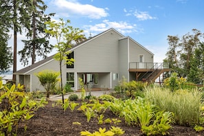 Ein modernes, zweistöckiges Haus mit Satteldach, einer Veranda und einem angelegten Garten mit verschiedenen Pflanzen.