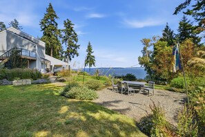 A house with a patio, a table, and chairs, overlooking a body of water.