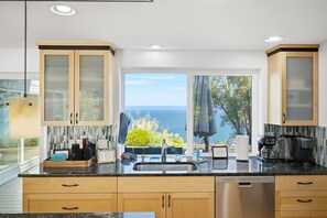 A modern kitchen with a large window offering a view of the sea.