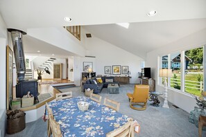 Un salón amplio con techo alto, chimenea, una mesa de comedor con mantel floral y vistas al exterior.