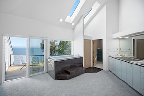 Una cocina moderna con una isla grande, un puerta corrediza de vidrio que da a un balcón y vistas al mar.