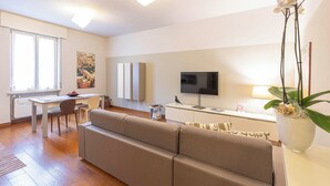 A modern living room with a sofa, a dining area with a table and chairs, a flat-screen TV, and a potted orchid. - VeronaLodge Bilo
Hospitality and Comfort in the Heart of Verona (Verona)