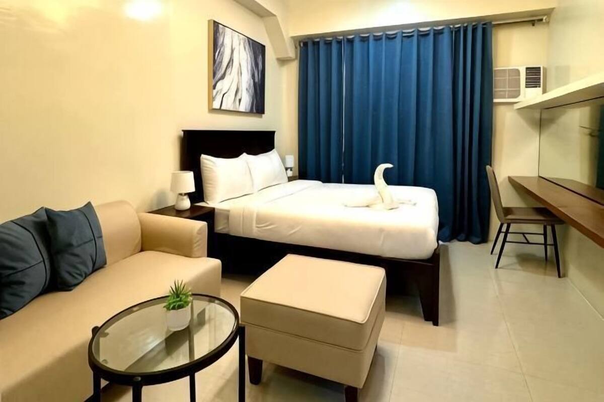 A hotel room with a bed, a sofa, a small table with a plant, a desk, and a chair.