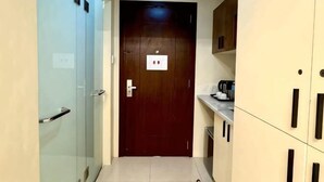 A narrow hallway with a wooden door, a glass door, and a kitchenette area with cabinets and a countertop. - G Square Residences (Manila)