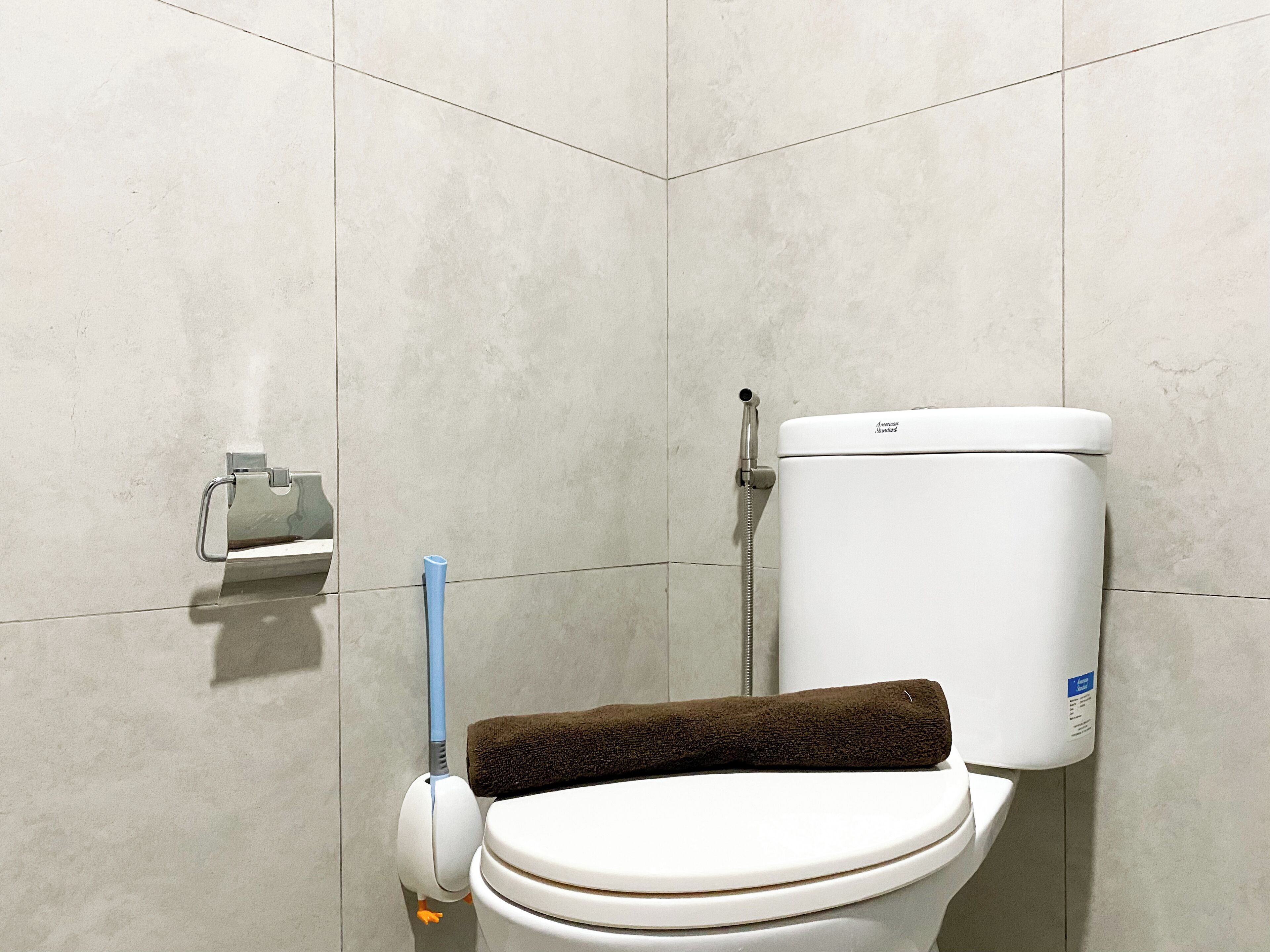 A toilet with a brown towel on the seat, a toilet paper holder, and a bidet spray.