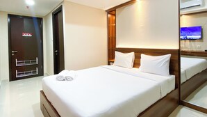 Ein Hotelzimmer mit einem großen Bett, einem Holzkopfstück, einem Spiegel, einem Fernseher und einer Tür mit Überwachungskamera.