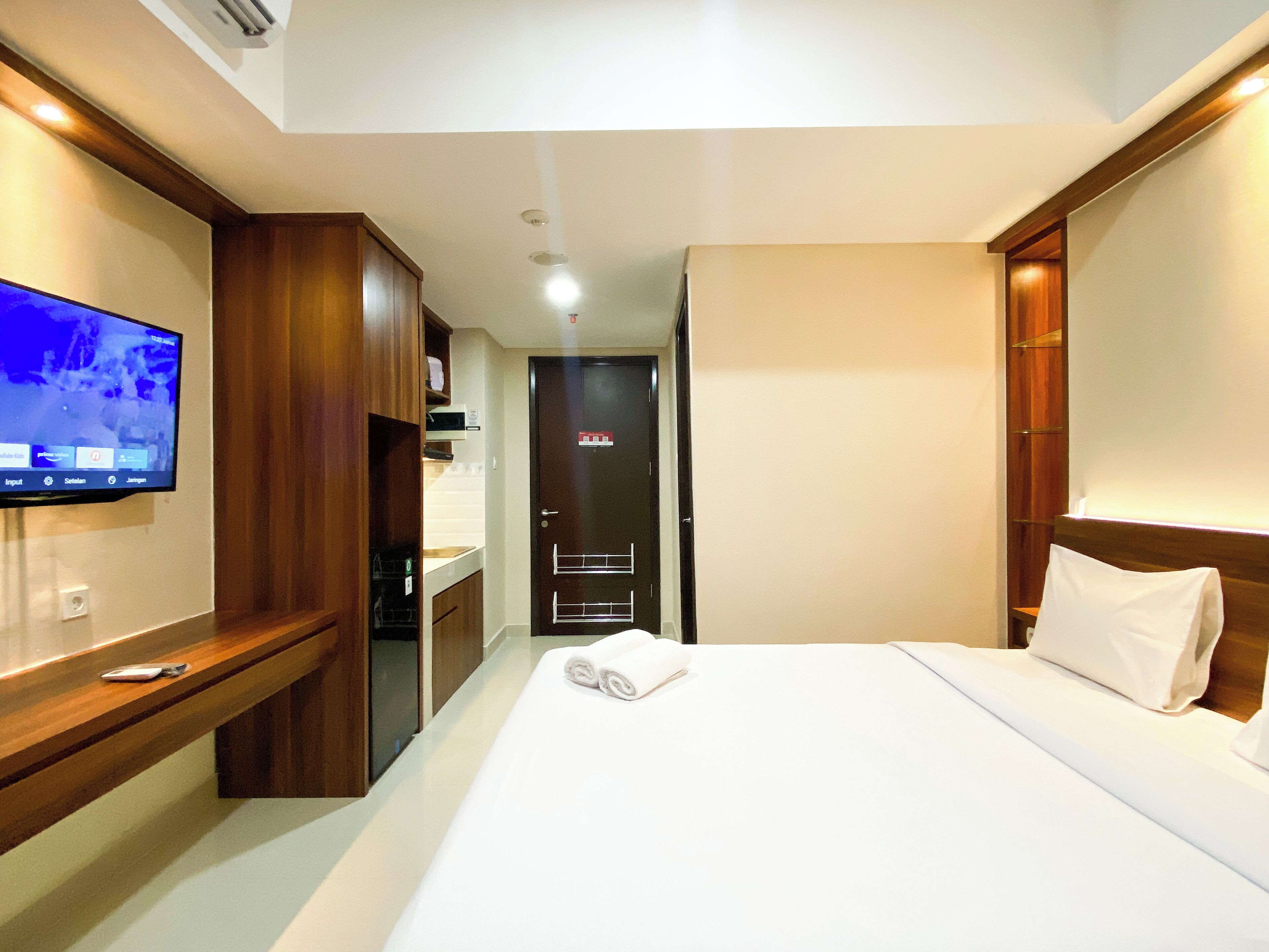 A hotel room with a bed, a TV on the wall, a wooden desk, and a door with a towel rack.