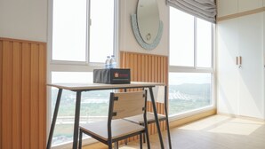 A room with a wooden paneled wall, a table with a chair, a large mirror, and a view of a bridge and greenery through the window. - Great Choice And Homey Studio Apartment At Tokyo Riverside Pik 2 (Teluknaga)