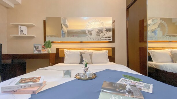 A hotel room with a bed, a mirror, a bookshelf, and a window with a view of a Ferris wheel. - Great Choice And Homey Studio Apartment At Tokyo Riverside Pik 2 (Teluknaga)