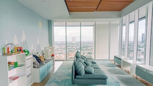 A modern living room with a grey sofa, white shelving, and a large window offering a city view. - Modern And Comfort 1Br At The Smith Alam Sutera Apartment (Tangerang)