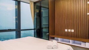 A hotel room with a large bed, a wooden panel wall, and a view through a large window. - Modern And Comfort 1Br At The Smith Alam Sutera Apartment (Tangerang)
