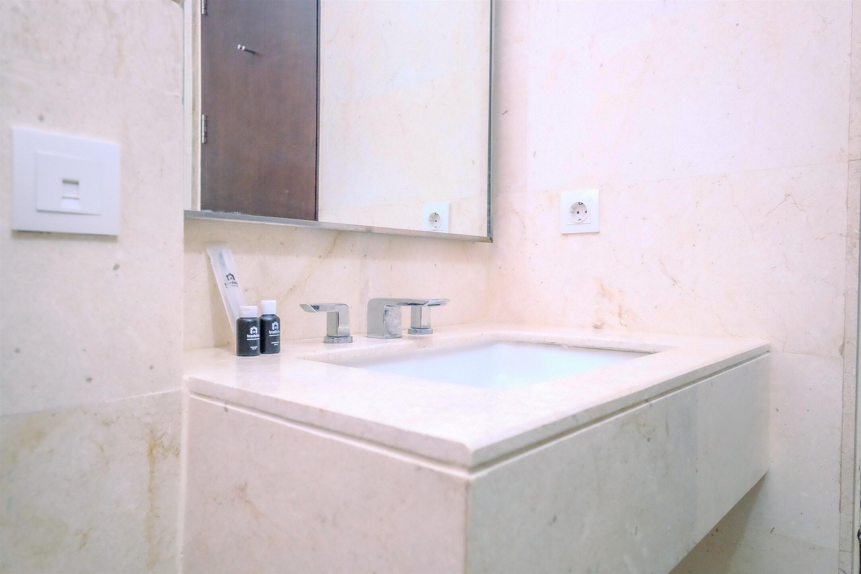 Un baño con un lavamanos blanco, dos grifos y un espejo encima. Hay dos botellas sobre la encimera del lavamanos.