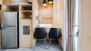 A compact kitchen with a refrigerator, a dining area with two chairs, a table, and pendant lights. - Strategic And Comfy Studio Apartment B Residence Near Bsd (Pagedangan)