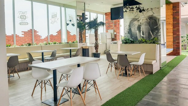 A modern restaurant with white tables and chairs, large windows, and a mural of an elephant. - Strategic And Comfy Studio Apartment B Residence Near Bsd (Pagedangan)