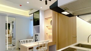A modern kitchen with a built-in stove, white bar stools, and a wooden cabinet. - Homey And Good Choice 2Br At Meikarta Apartment (Cikarang)