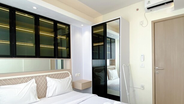 A hotel room with a bed, a mirror, a wardrobe, and a door. - Homey And Good Choice 2Br At Meikarta Apartment (Cikarang)
