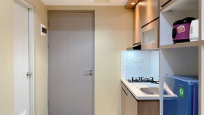 A compact kitchen with a built-in gas stove, a microwave, and a refrigerator. - Minimalist And Enjoy Living 1Br Vasanta Innopark Apartment (Cikarang)