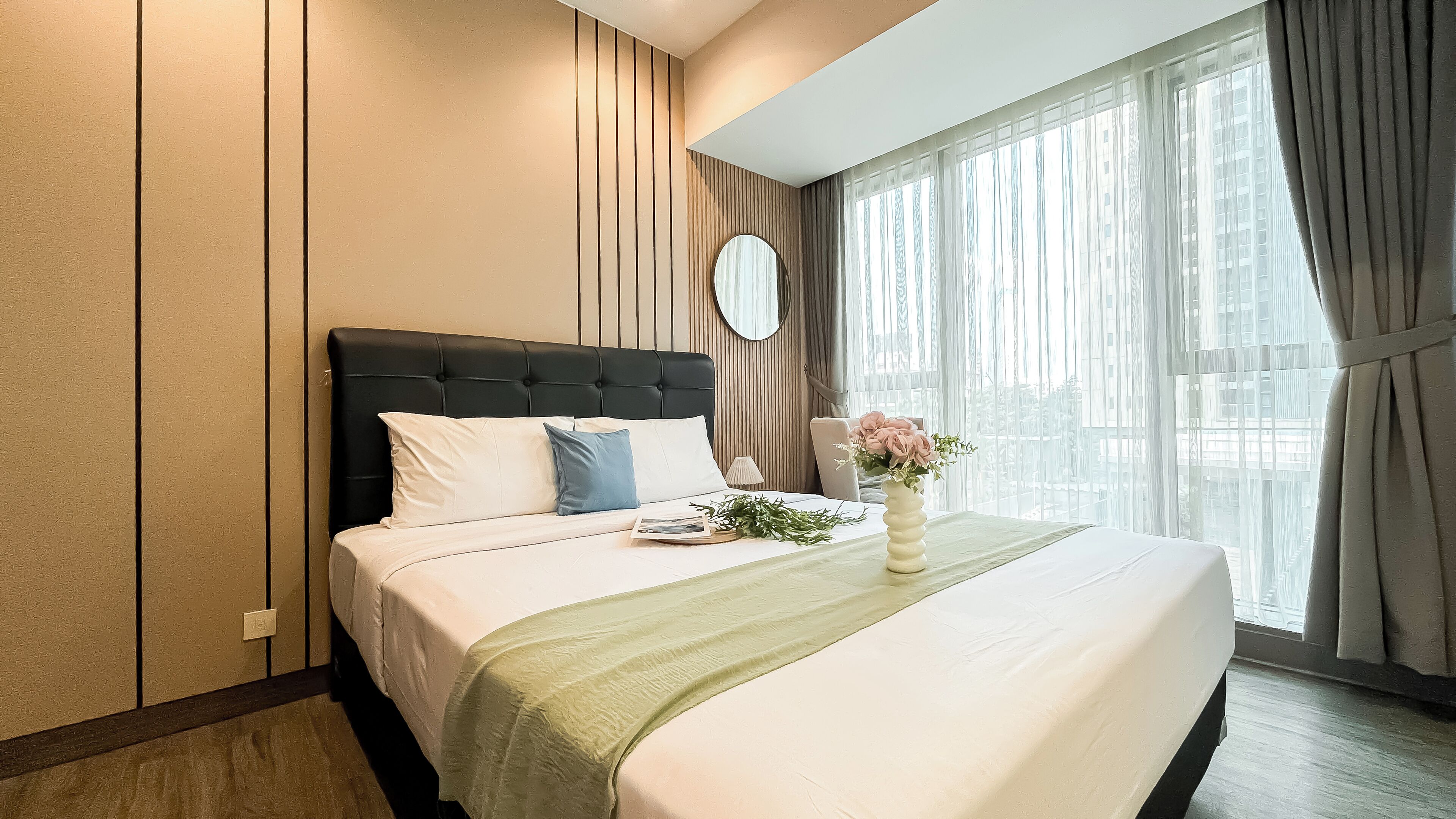 A hotel room with a large bed, a bedside table with a lamp, a mirror, and a window with curtains.
