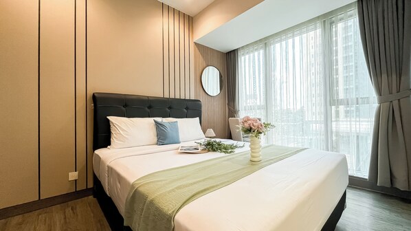 A hotel room with a large bed, a bedside table with a lamp, a mirror, and a window with curtains. - Modern 2Br Branz Bsd City Apartment Near Aeon Mall (Pagedangan)
