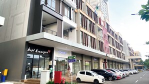 A multi-story building with a coffee shop named "Kopi Kenangan" on the ground floor, a sign for "Tomoro Coffee" above it, and a row of parked cars along the street. - Good Place 1Br Vasanta Innopark Apartment (Cikarang)