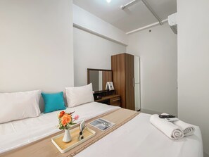 Une chambre d’hôtel avec un lit, une armoire en bois, un bureau avec un miroir et une petite table sur laquelle est posé un vase de fleurs.