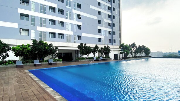 A modern building with a swimming pool, surrounded by greenery and lounge chairs. - Good Place 1Br Vasanta Innopark Apartment (Cikarang)