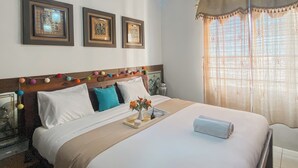 A neatly made bed with a tray of flowers, a vase, and a rolled towel. There are three framed pictures on the wall above the bed. - Warm And Homey 2Br At Marina Ancol Apartment (Jakarta)