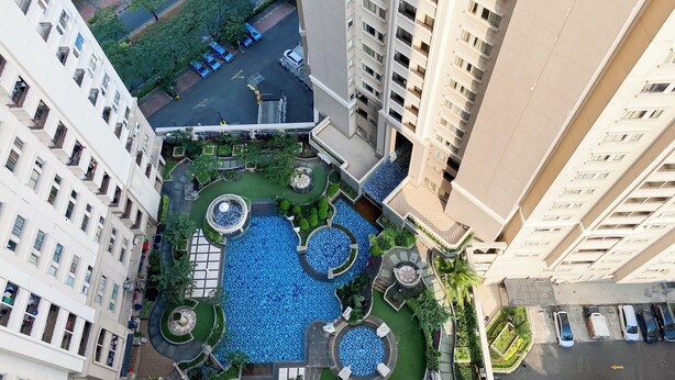 A high-rise building with a rooftop garden featuring a central pool, surrounded by pathways and seating areas. - Warm And Homey 2Br At Marina Ancol Apartment (Jakarta)