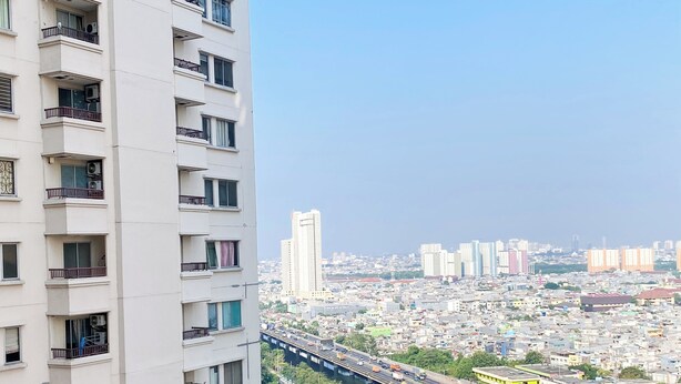 A high-rise building with multiple balconies and a view of a busy cityscape with a river and a bridge. - Warm And Homey 2Br At Marina Ancol Apartment (Jakarta)