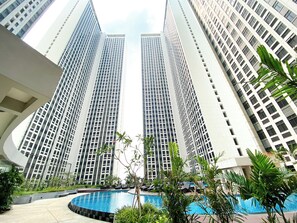 Un hôtel moderne doté d’une piscine centrale, entouré d’une végétation luxuriante et avec de grands immeubles en arrière-plan.