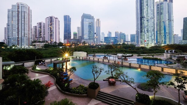 Un área de piscina en la azotea con vistas a un paisaje urbano, rodeada de vegetación y edificios modernos.