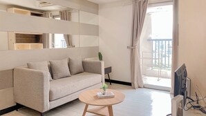 Una sala de estar moderna con un sofá, una mesa redonda de centro, un televisor y un balcón con cortinas.