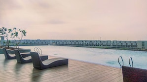 A poolside area with lounge chairs and a view of a modern building across the water. - Modern 2Br At Vasanta Innopark Apartment (Cikarang)