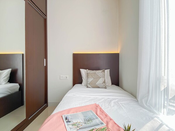Une chambre d’hôtel comprenant un lit, une table de chevet, une armoire et une fenêtre avec des rideaux légers.