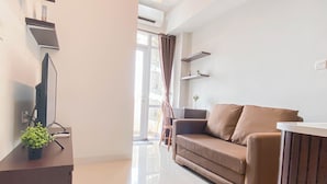 A modern living room with a brown sofa, a flat-screen TV, and a small plant on a wooden table. - Modern 2Br At Vasanta Innopark Apartment (Cikarang)
