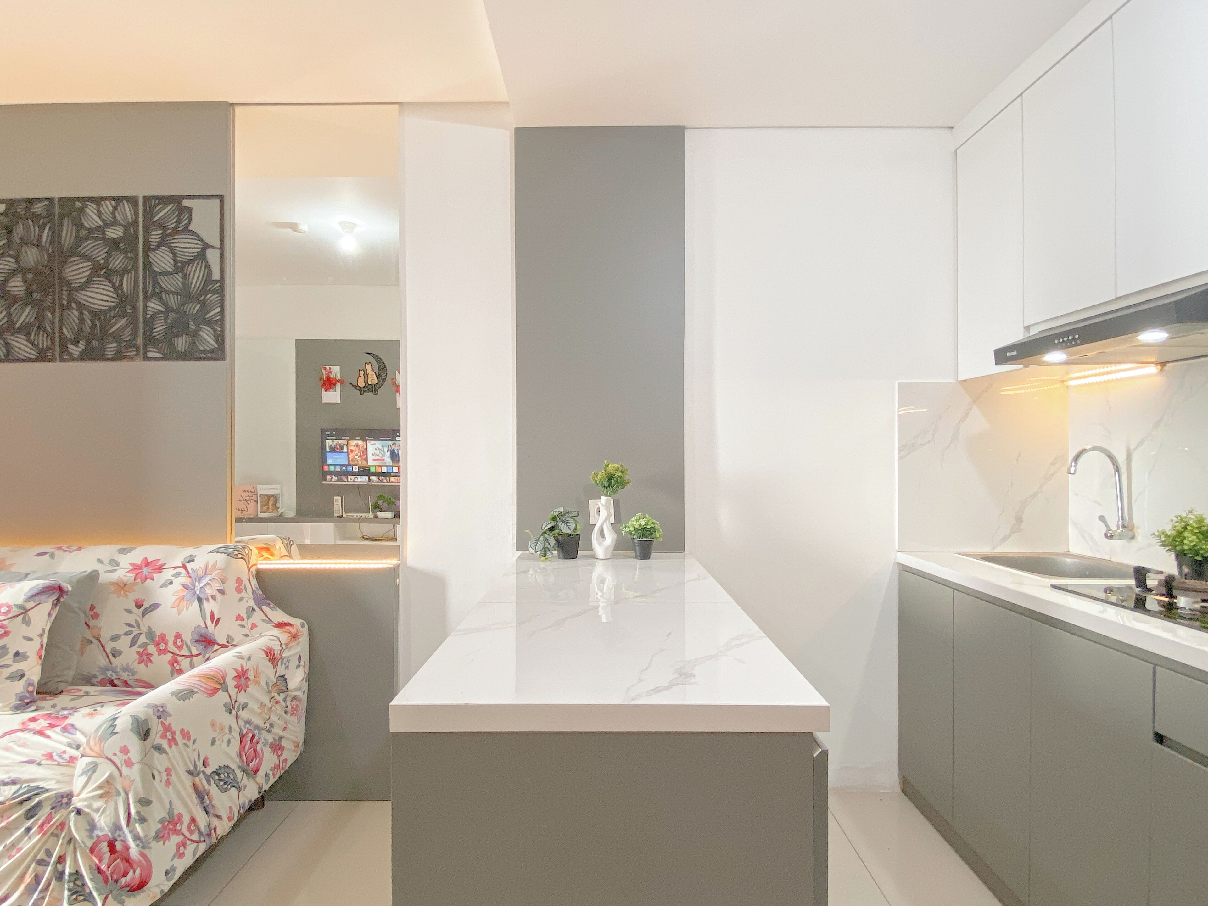 A modern kitchen with a central island, grey cabinets, and a built-in TV.