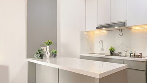Uma cozinha moderna com bancada branca, pia embutida e torneira de aço inoxidável. Há três vasos com plantas na bancada.