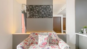Um quarto acolhedor com um sofá estampado com flores, um painel decorativo na parede e uma pequena planta numa prateleira.
