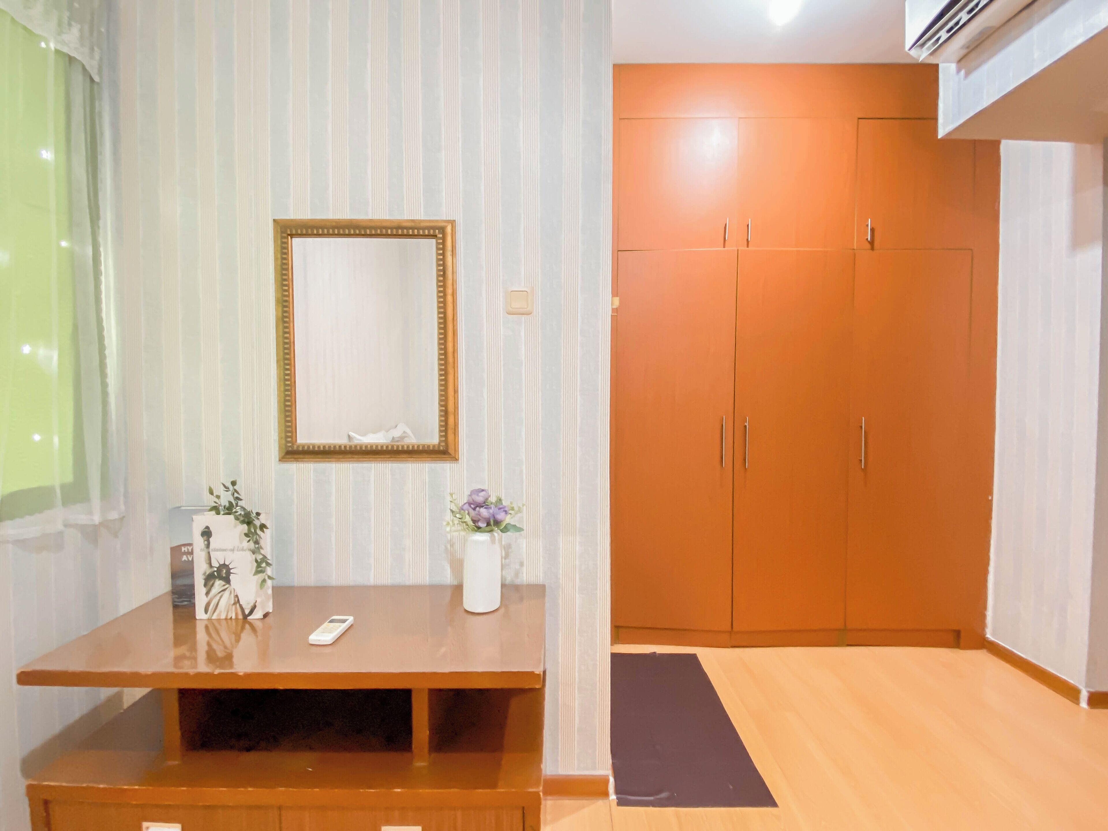 A room with a wooden desk, a mirror, a vase with flowers, and a wardrobe.