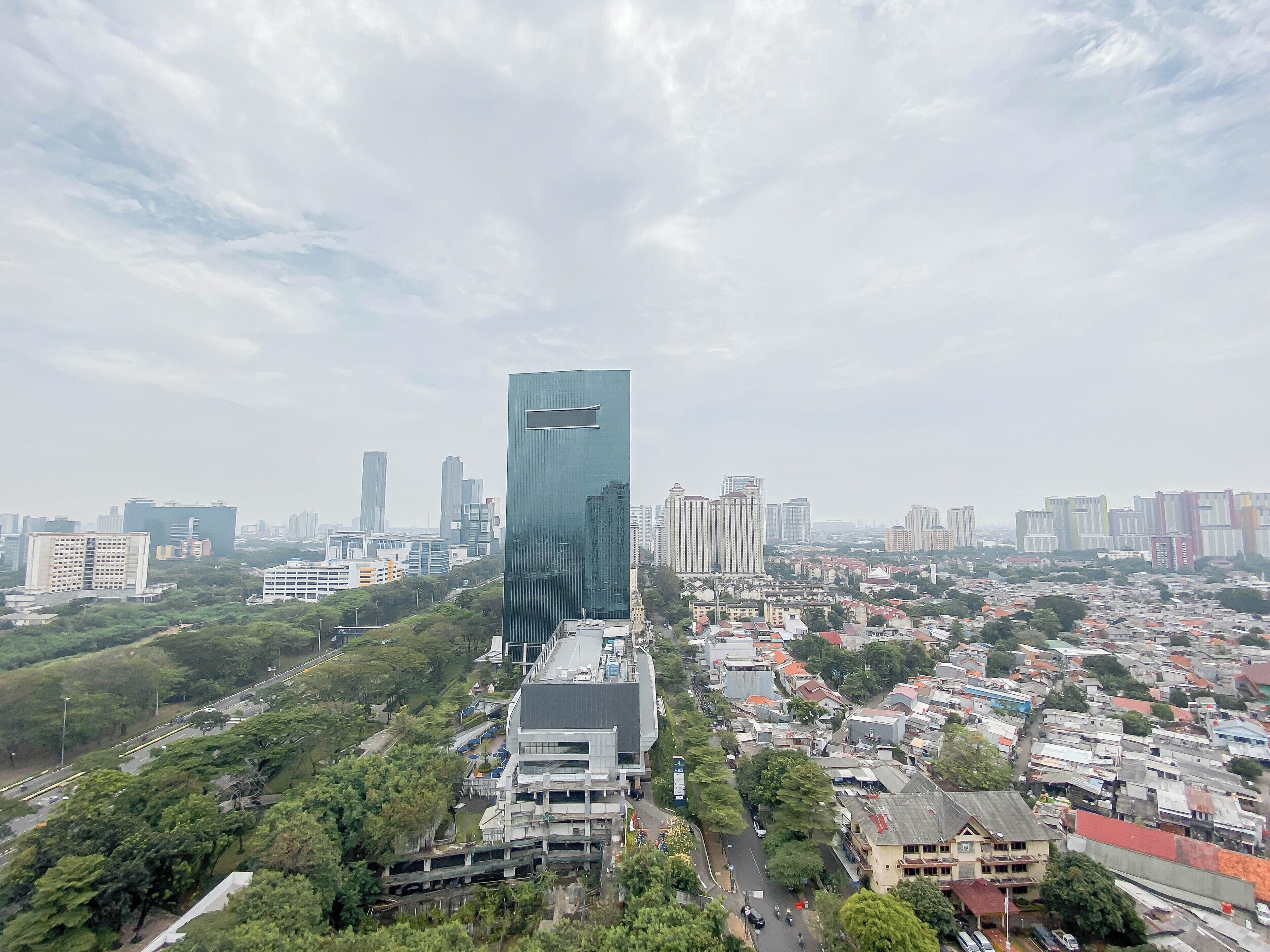 Un edificio de gran altura con fachada de vidrio moderna, rodeado de edificios residenciales y comerciales, bajo un cielo despejado.