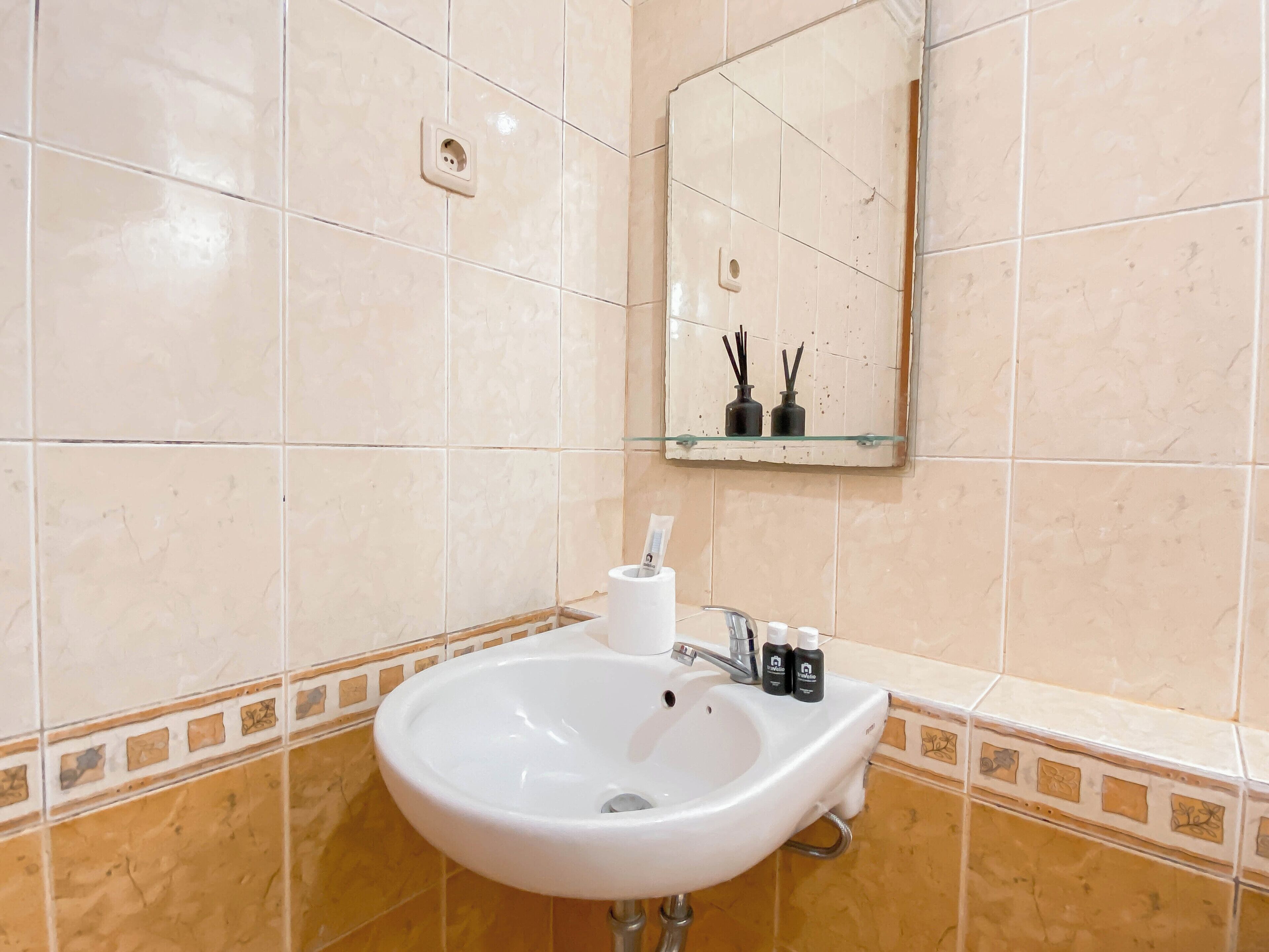 Une salle de bain avec un lavabo blanc, un miroir et une petite étagère sur laquelle sont posées deux bouteilles.