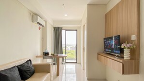 A modern living room with a sofa, a TV, and a small table with a vase of flowers. - Scandinavian Minimalist 2Br Apartment At Daan Mogot City (Jakarta)