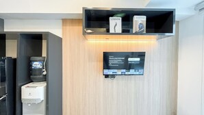Ein modernes Hotelzimmer mit Wasserspender, einem an einer Holzwand montierten Flachbildfernseher und einem Bücherregal.
