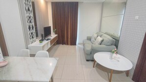 A modern living room with a sofa, a coffee table, a TV, and a dining area with a table and chairs. - 1Br Near Mall At Grand Sungkono Lagoon Apartment (Surabaya)