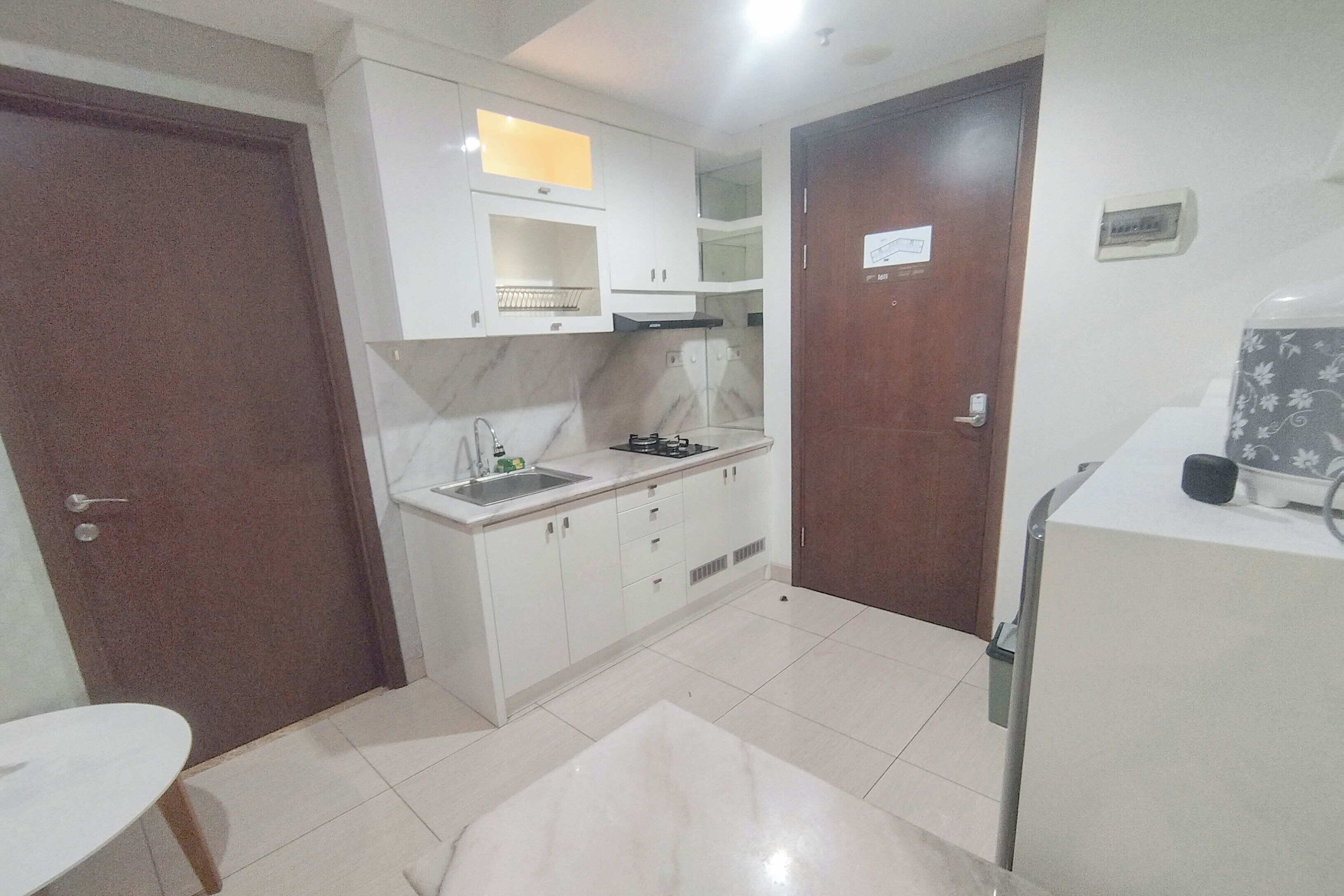 Cocina compacta con armarios blancos, un lavamanos y una estufa. Hay una puerta de madera y una encimera blanca con un microondas.