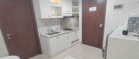 Cocina compacta con armarios blancos, un lavamanos y una estufa. Hay una puerta de madera y una encimera blanca con un microondas.
