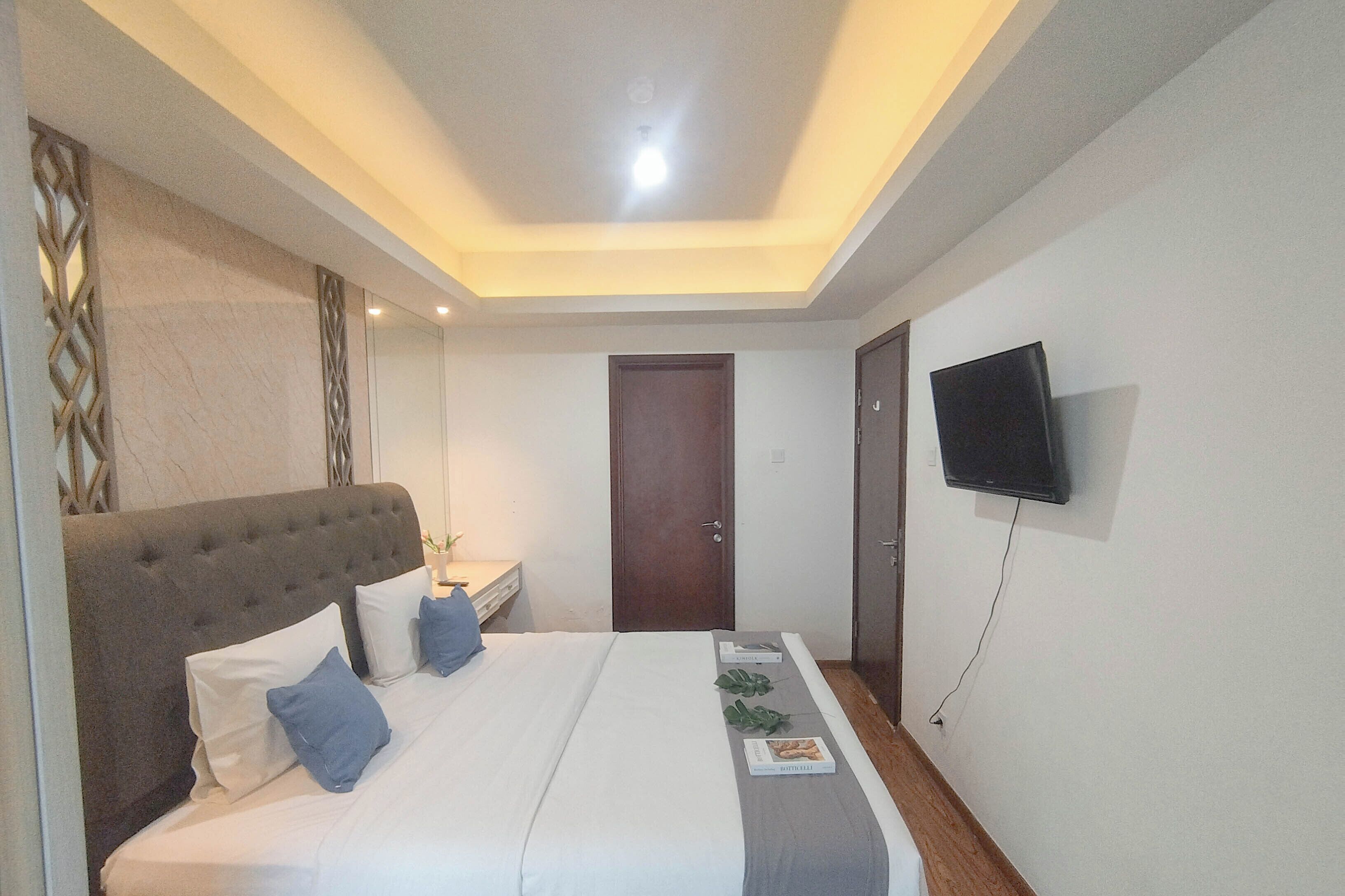 A hotel room with a large bed, a flat-screen TV mounted on the wall, and a door in the background.