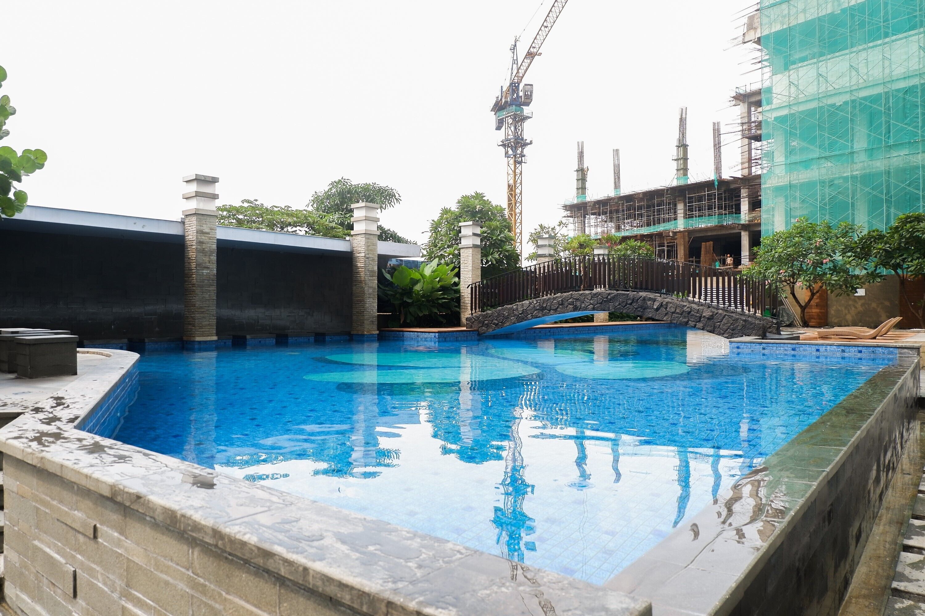 A swimming pool with a stone border, a stone bridge, and a construction site in the background.